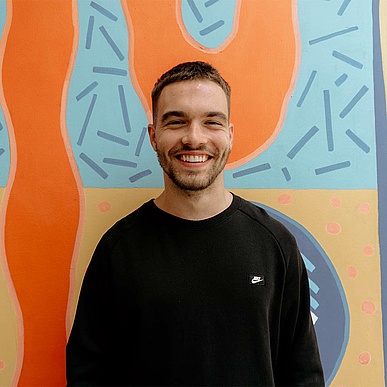 Young professional standing in front of a colourful wall and grinning