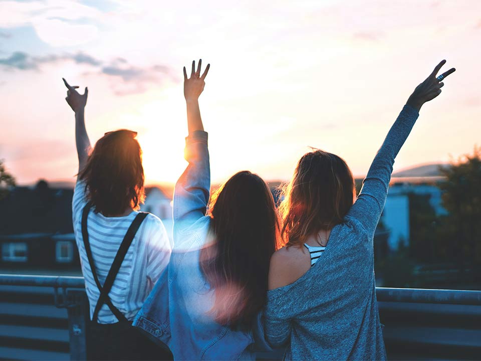 Tres mujeres miran la puesta de sol y sostienen sus manos en el aire
