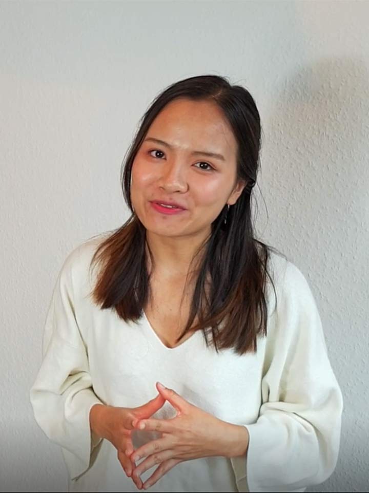 Joven mujer asiática se para delante de una pared blanca y sonríe