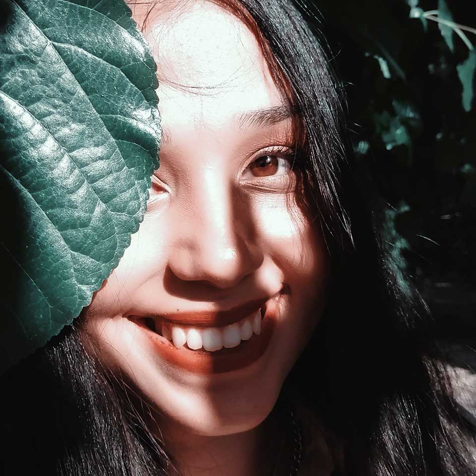 Joven mujer asiática sonriendo a la cámara con una hoja de la planta delante de su rostro