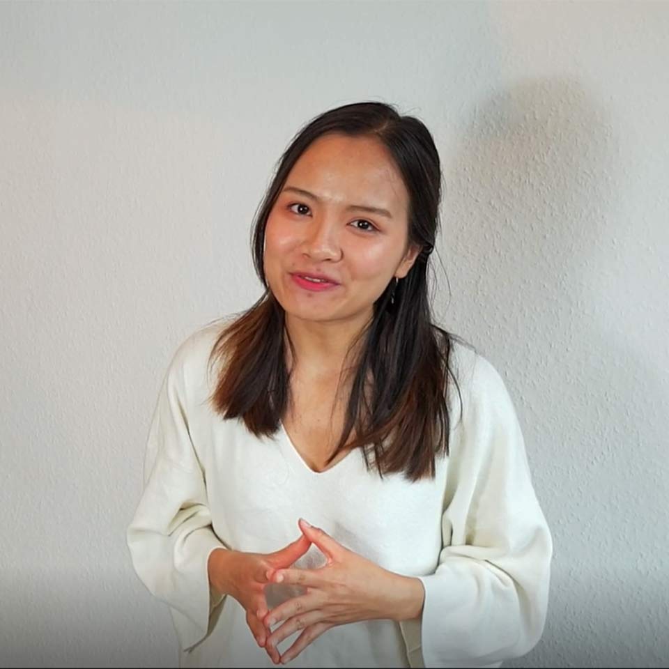 Joven mujer asiática se para delante de una pared blanca y sonríe 